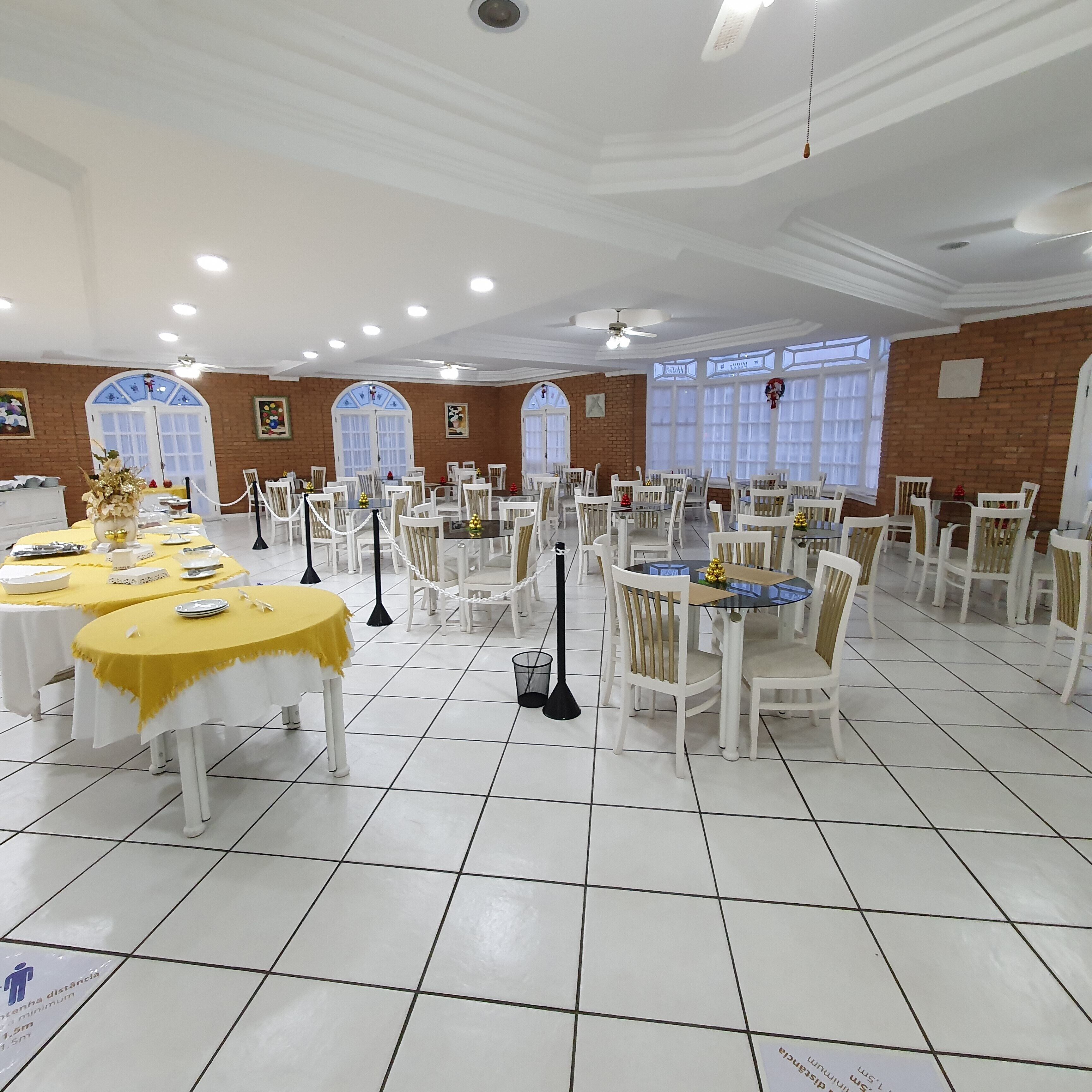 A spacious banquet hall with multiple round tables, white chairs, and a tiled floor.