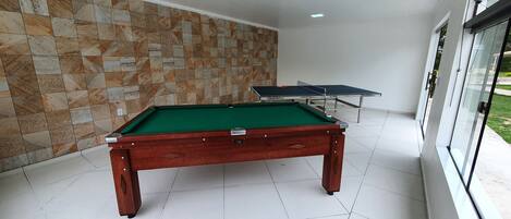 A pool table with a green felt surface, a wooden frame, and a drawer. There is a wall with a patterned tile design behind it.