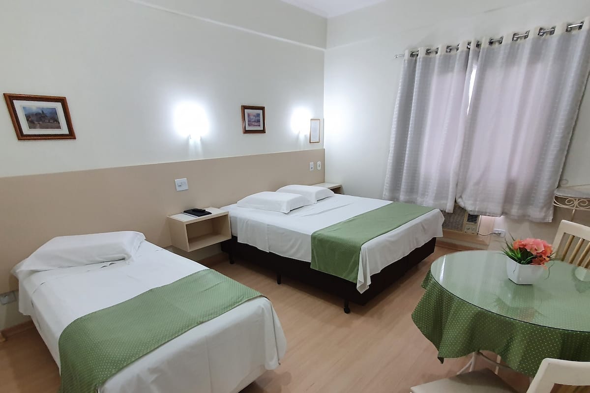 A hotel room with two beds, a small table with a vase of flowers, and a chair.