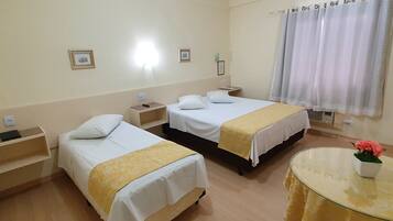 Habitación de hotel con dos camas, una mesa redonda con un florero y una ventana con cortinas.