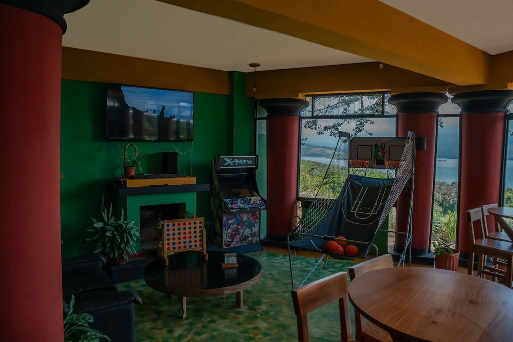Una habitación con una pared verde, un televisor de pantalla plana, una consola de videojuegos, una hamaca y vistas al exterior.