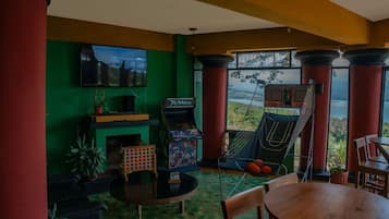 A room with a green wall, a flat-screen TV, a gaming console, a hammock, and a view of the outdoors.