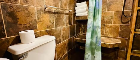 A bathroom with a toilet, a roll of toilet paper, a shower curtain, and a towel rack with towels.