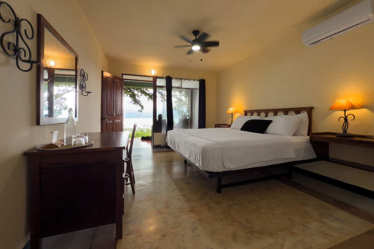 A bedroom with a bed, bedside tables, a desk, a chair, a ceiling fan, and a view through a glass door.