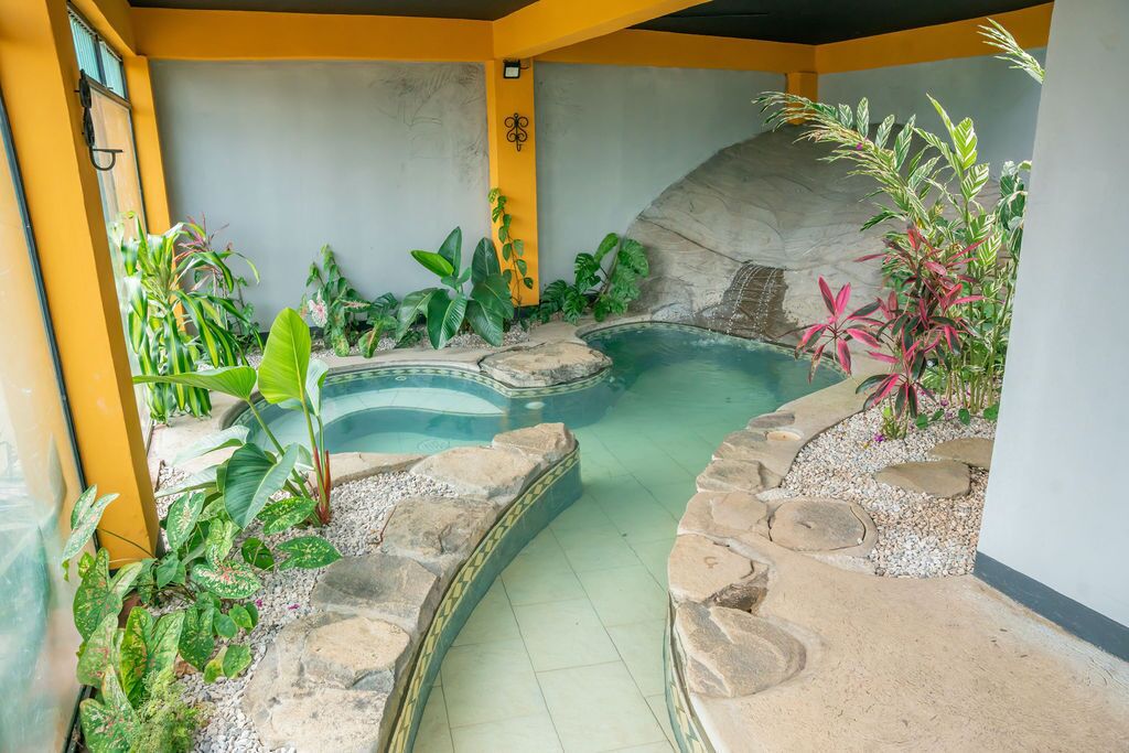 A swimming pool surrounded by tropical plants and stone tiles.