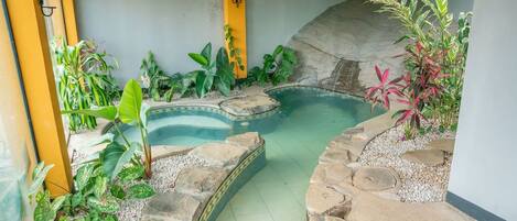 A swimming pool surrounded by tropical plants and stone tiles.