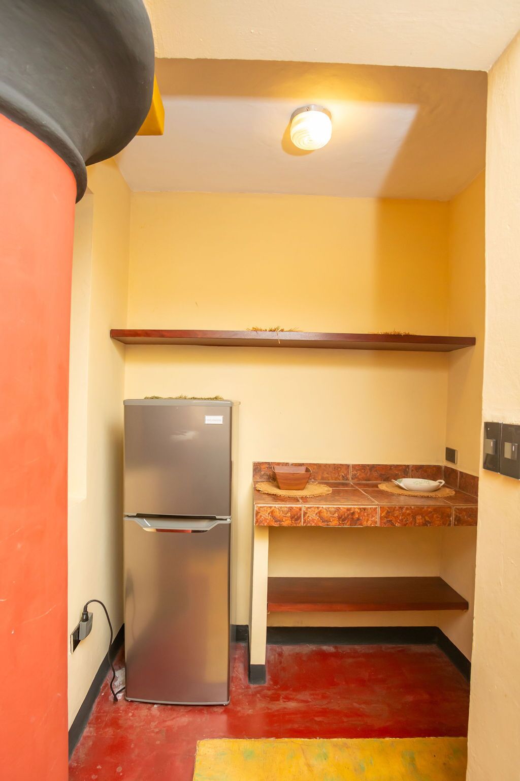 Una cocina compacta con un refrigerador, una encimera con un tazón y un estante arriba.