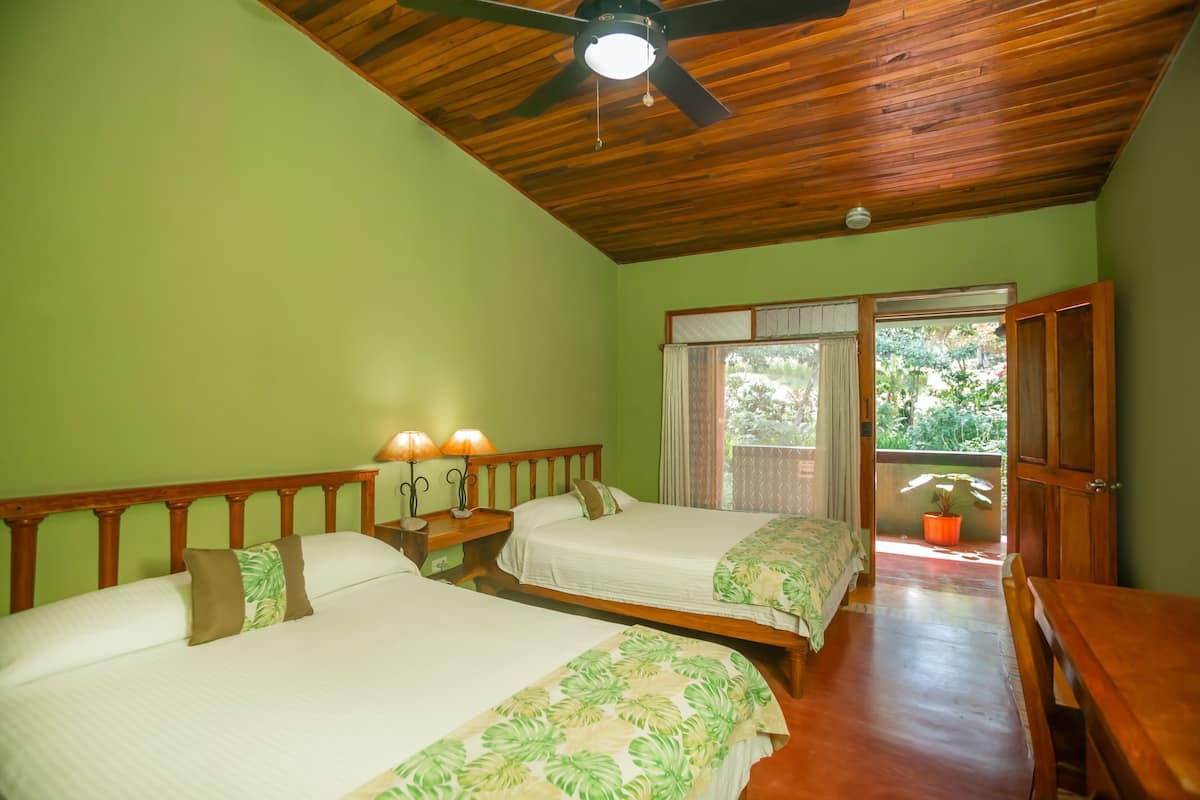 A room with two beds, wooden ceiling, and a view of greenery outside.