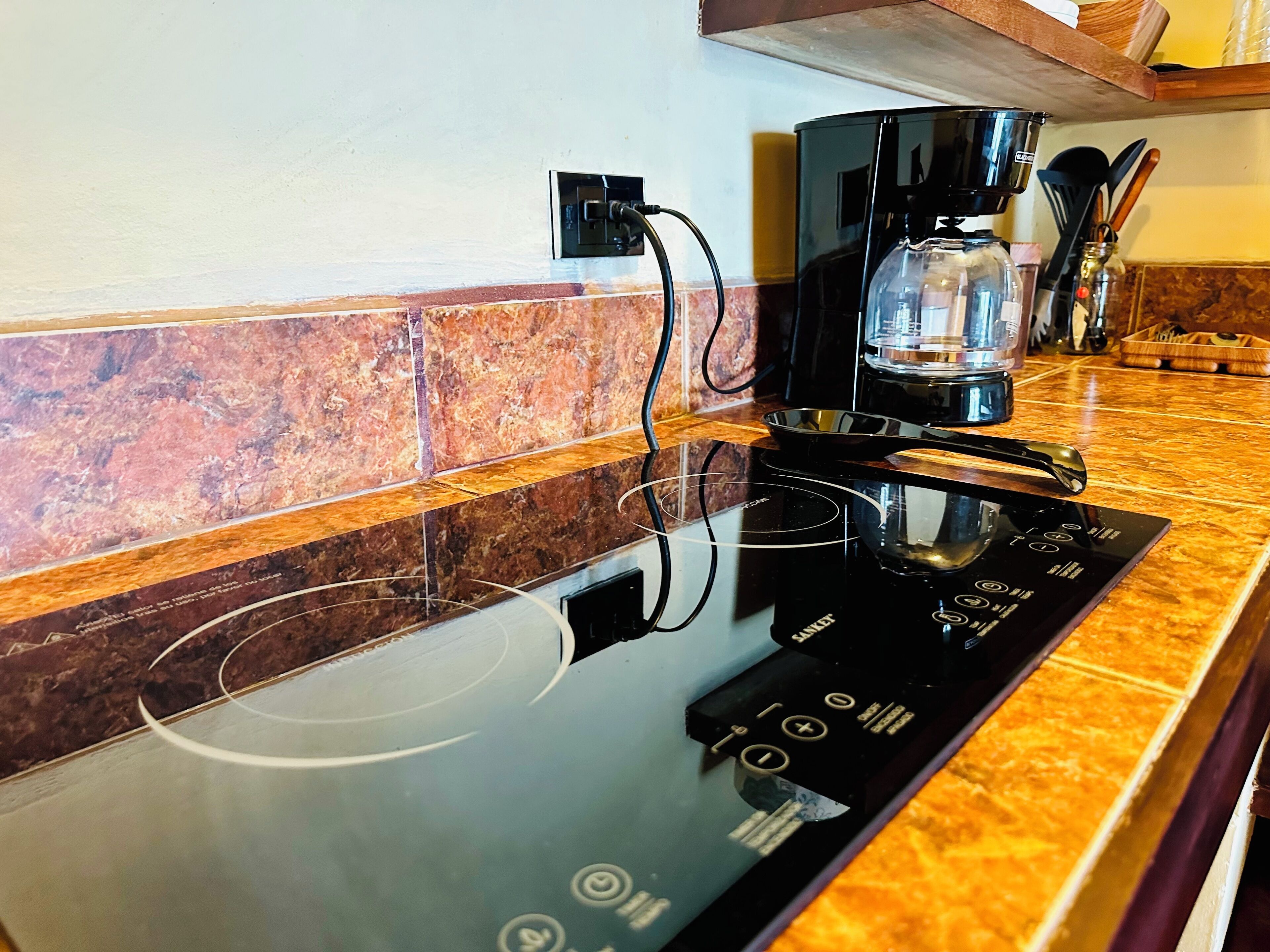 Una cocina con una placa de inducción negra, una cafetera y un recipiente de vidrio sobre la encimera.