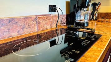 Una cocina con una placa de inducción negra, una cafetera y un recipiente de vidrio sobre la encimera.
