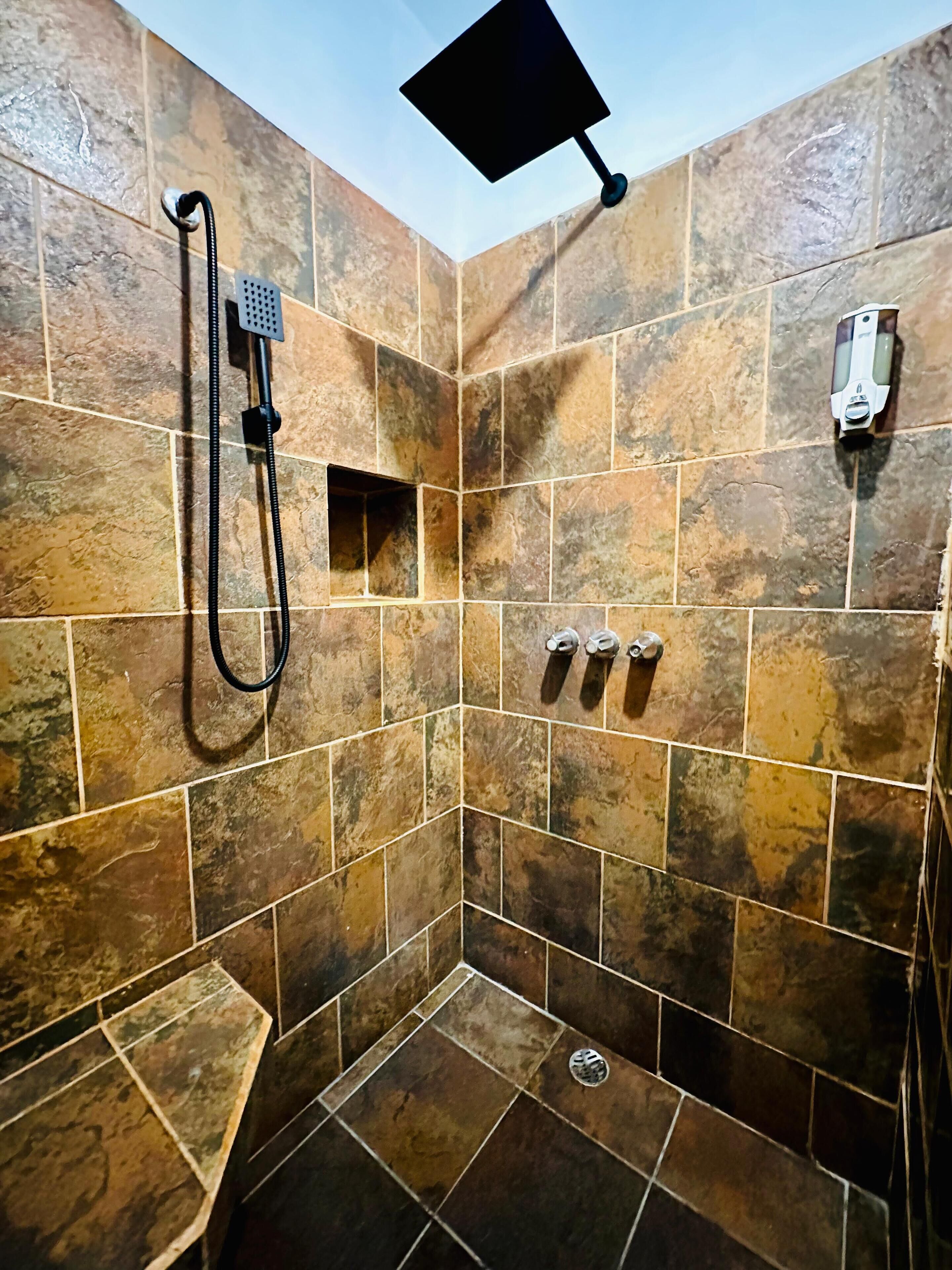 A shower area with a handheld showerhead, a square showerhead, and a handheld soap dispenser.