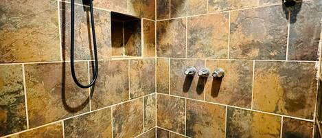 A shower area with a handheld showerhead, a square showerhead, and a handheld soap dispenser.