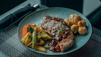 Un plato de comida con un filete, verduras y dumplings sobre un mantel tejido.