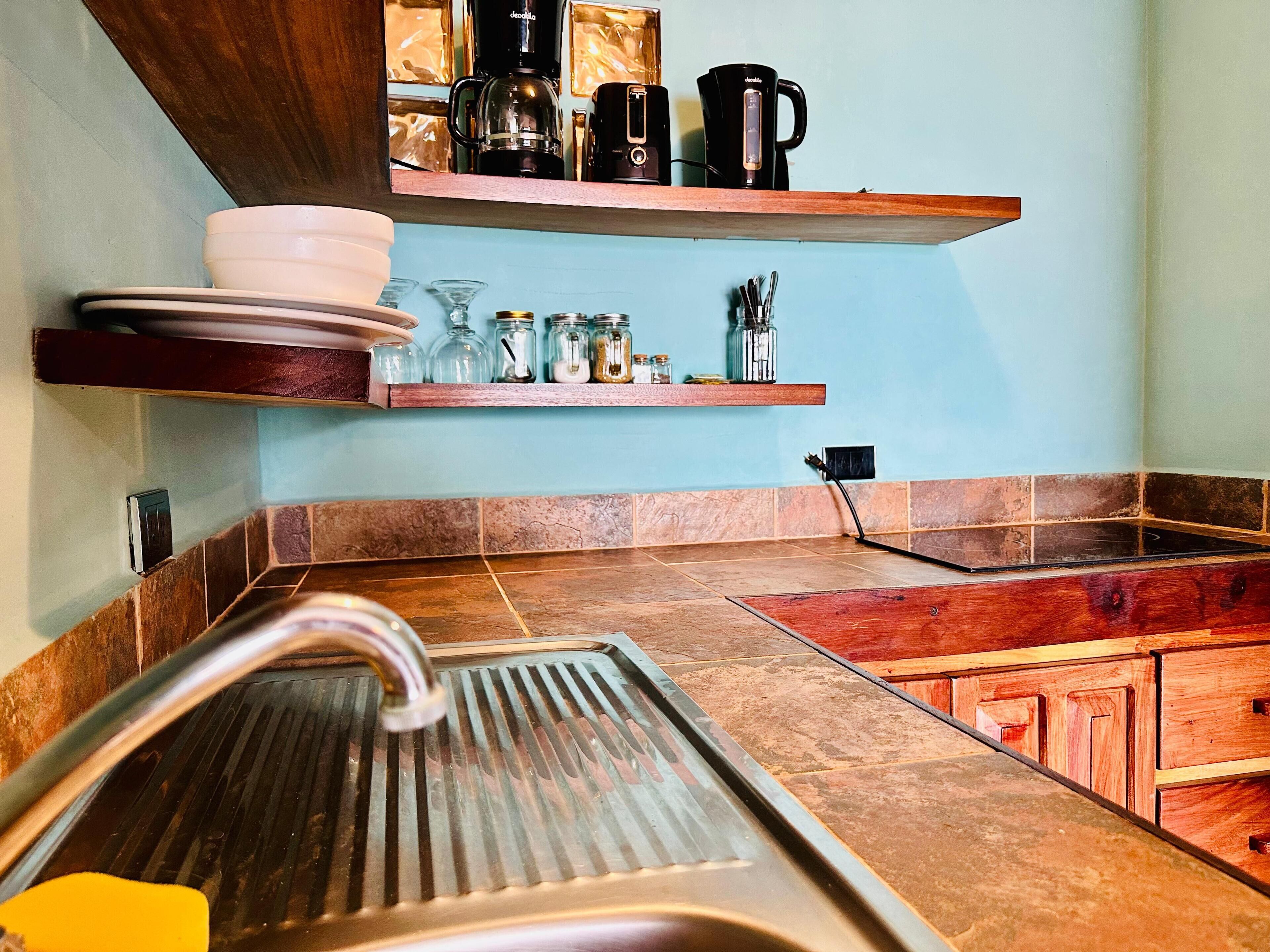 Une cuisine dotée d’un évier en acier inoxydable, de meubles de rangement en bois et d’un plan de travail sur lequel se trouvent une machine à café et des bocaux.