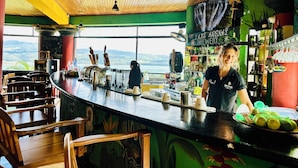 A bar with a counter, chairs, and a view of the mountains. - Lake Arenal Hotel, Brewery & Farm (Santa Rosa)