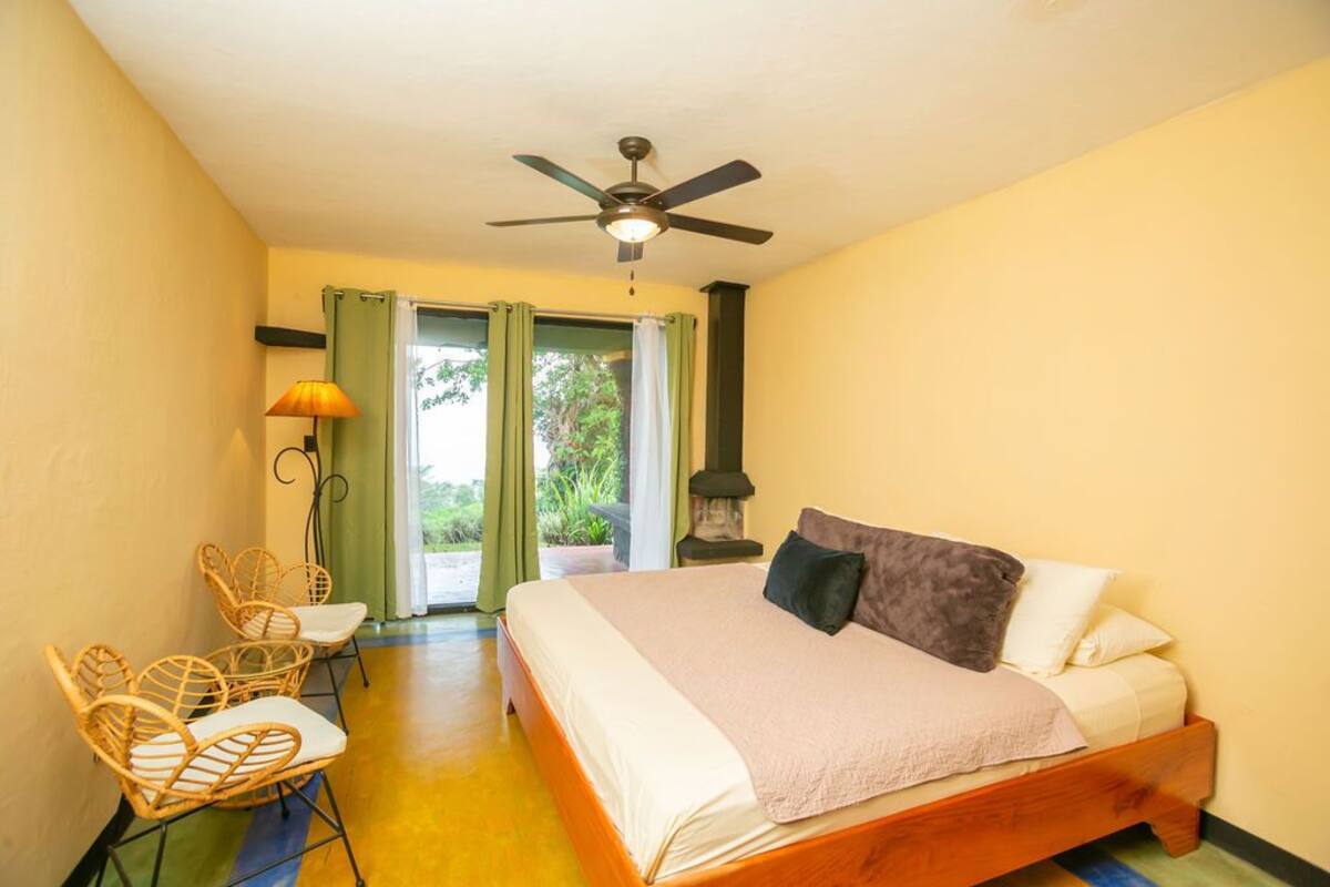 A bedroom with a bed, a ceiling fan, a window with curtains, and a chair.