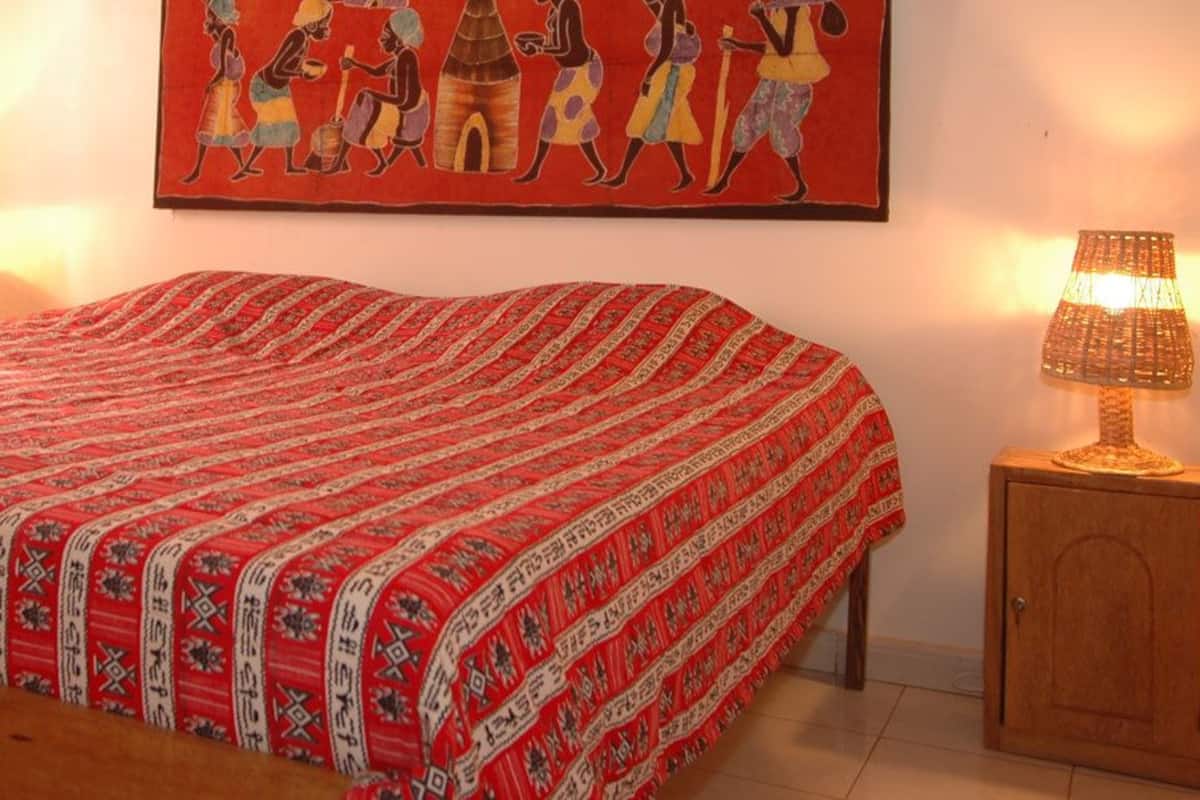 A bedroom with a bed, two bedside lamps, a wooden nightstand, and a wall painting.
