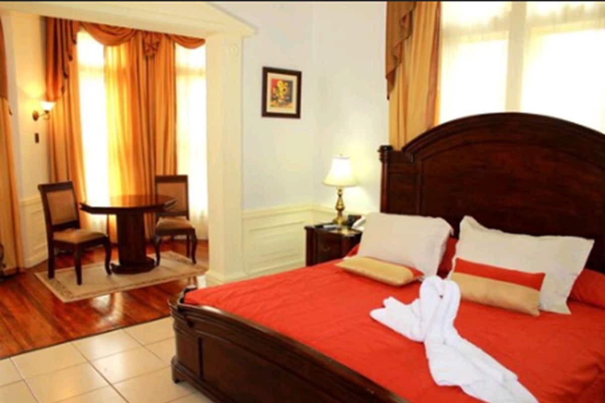 Een hotelkamer met een houten bed, rode beddengoed, een witte badjas, een klein tafeltje met stoelen en een lamp.