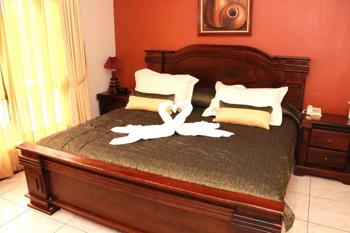 Een net opgemaakt bed met een zwaanvormige handdoek, een houten hoofdbord en een nachtkastje met een lamp.