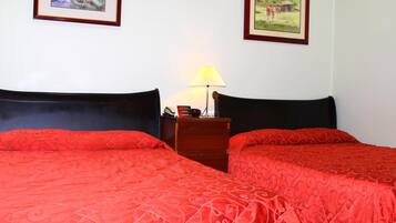 Una habitación con dos camas, cada una con una colcha estampada roja, una mesita de noche de madera con una lámpara, y dos cuadros enmarcados en la pared.
