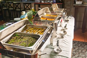 Een buffetopstelling met diverse etenswaren in metalen bakken, een ananas en een witte tafelkleed.