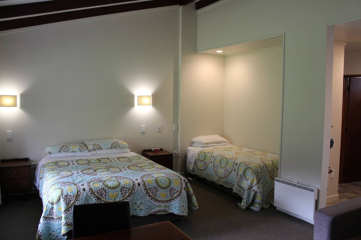 Habitación de hotel con dos camas, un escritorio y una silla. Hay luces fijadas a la pared y un calentador.