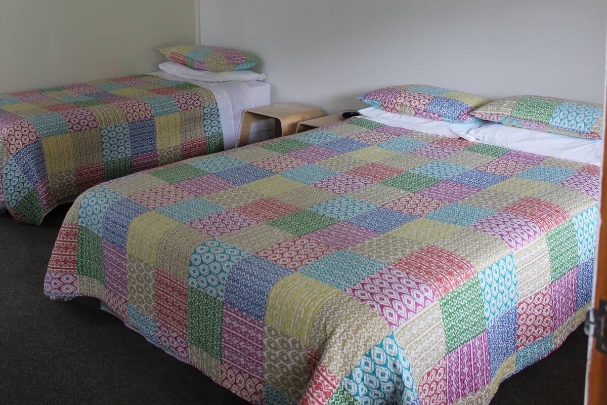 Una habitación con dos camas, cada una con un edredón colorido, una mesita pequeña y dos lámparas fijadas a la pared.