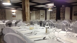 Een balzaal met lange tafels gedekt voor een formeel evenement, met witte tafelkleden, bestek en wijnglazen.