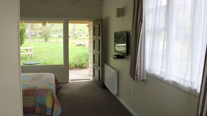 Een kamer met een bed, een televisie aan de muur, een raam met gordijnen en een open deur naar een tuin.
