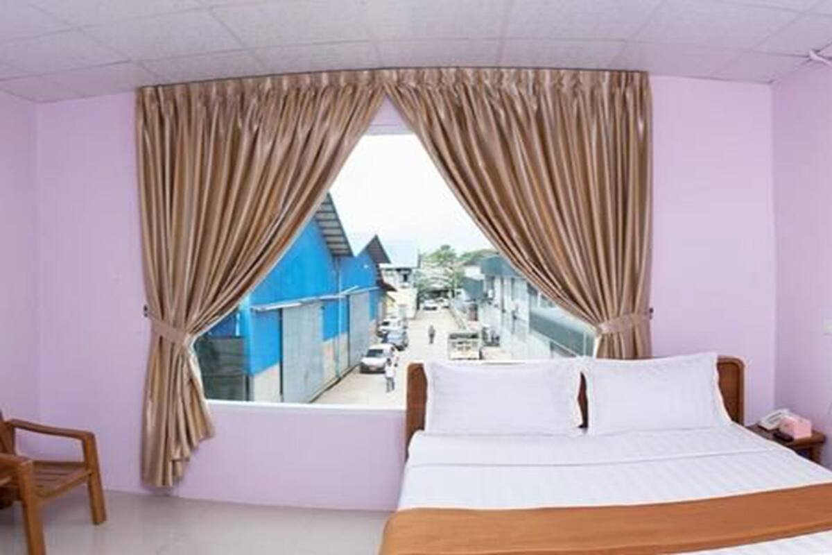 A bedroom with a bed, curtains, a chair, and a view of a street outside.
