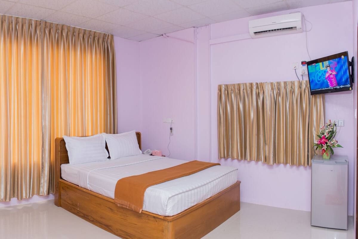 A hotel room with a wooden bed, a television on the wall, and a small refrigerator.