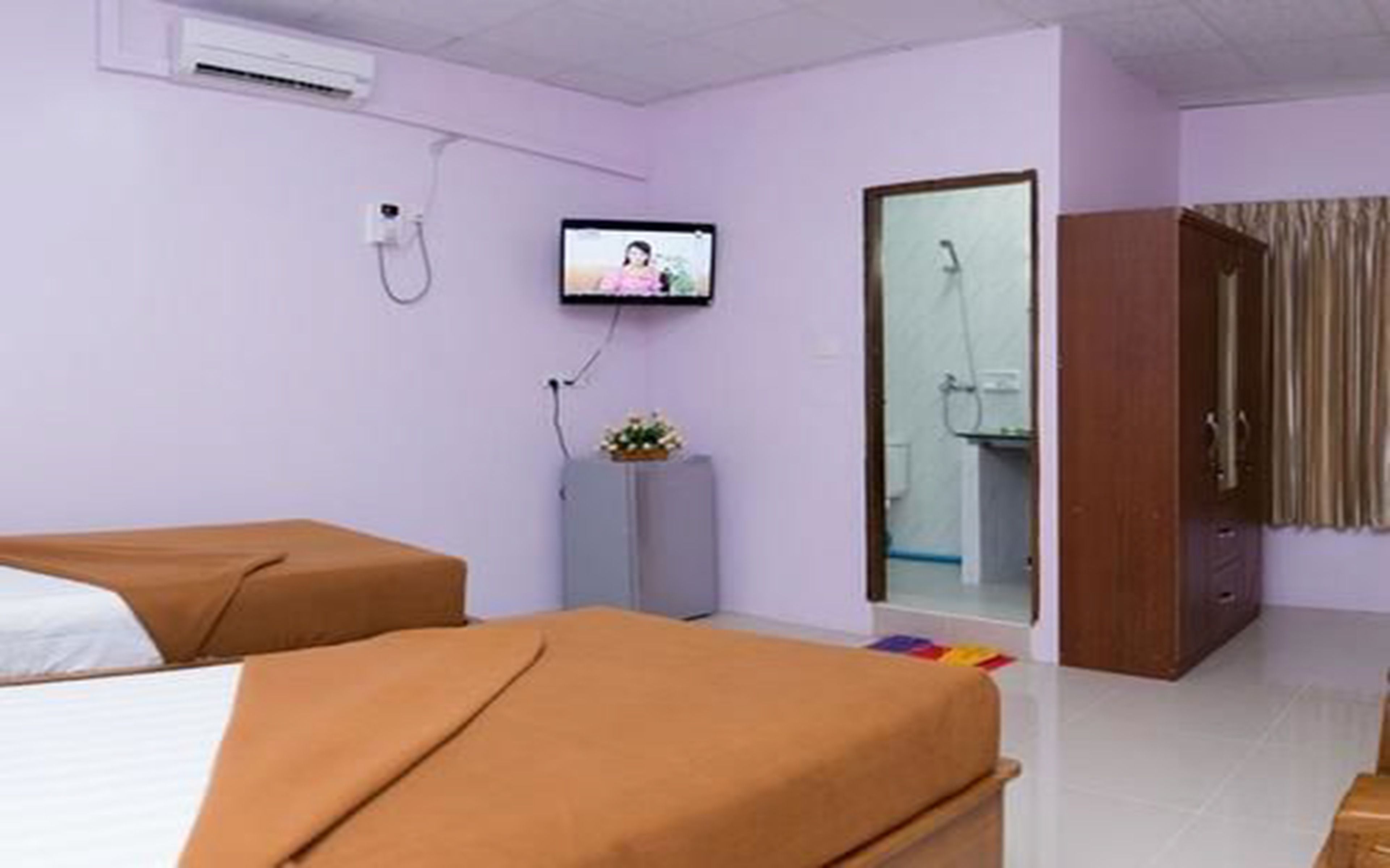 Habitación de hotel con dos camas, televisión, armario y un pequeño aparador con un arreglo floral.