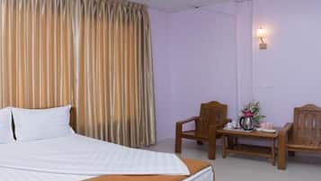 A hotel room with a bed, a wooden chair, a small table with a vase of flowers, and a wall-mounted lamp.