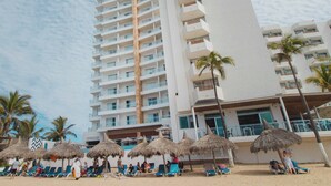 A high-rise hotel with multiple balconies, a beach area with lounge chairs and thatched umbrellas, and palm trees. - Pacific Palace Beach Tower Hotel (Mazatlán)