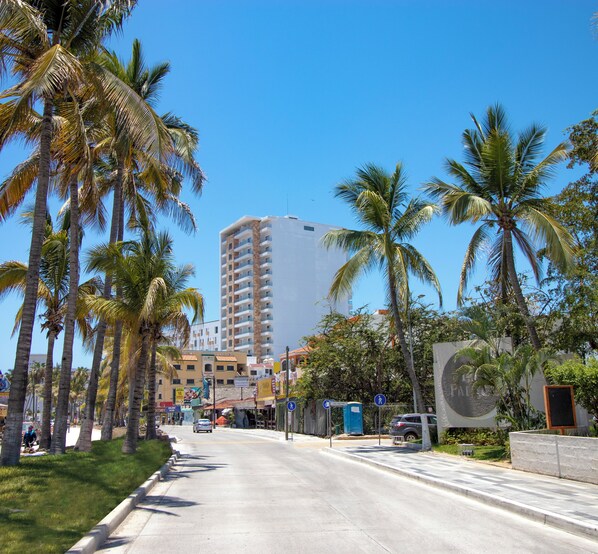 A street lined with palm trees and a tall building in the background. - Pacific Palace Beach Tower Hotel (Mazatlán)