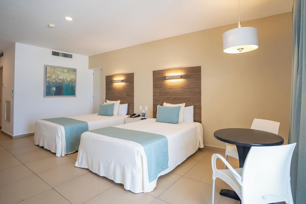 A hotel room with two beds, a small table, and a chair.
