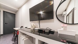 Un baño moderno con un espejo grande, un televisor de pantalla plana sobre el lavamanos y un perchero para toallas.