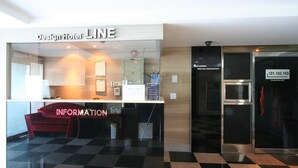 Zona de recepción de hotel con mostrador de check-in, un mostrador de información rojo y una cámara de seguridad.