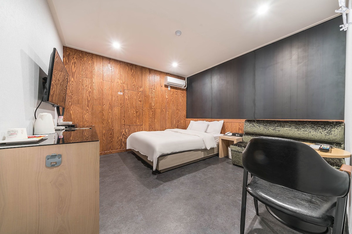 Una habitació d'hotel amb llit, escriptori, cadira, televisió i aire condicionat.