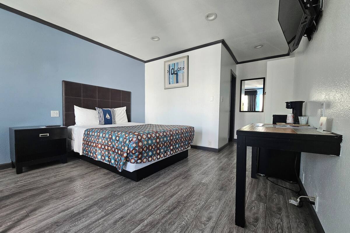 A hotel room with a bed, a desk, a chair, a TV, and a painting on the wall.