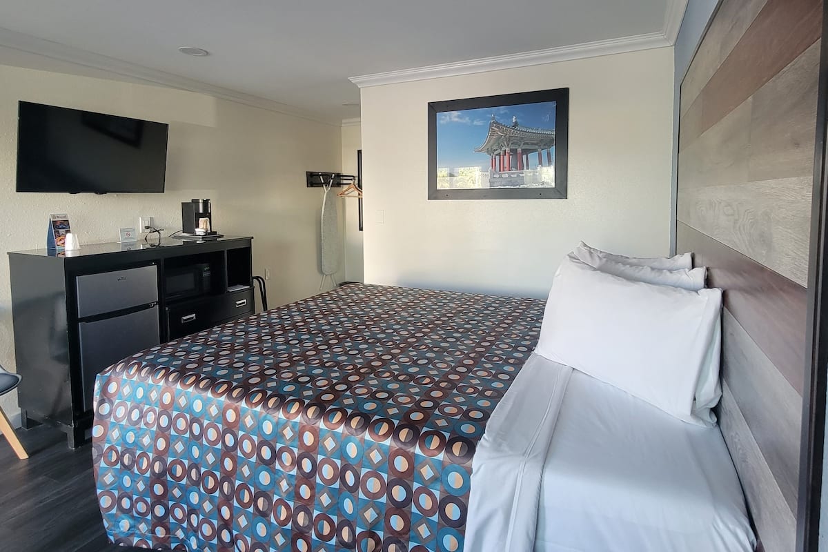 A hotel room with a large bed, a desk, a flat-screen TV, and a framed picture on the wall.