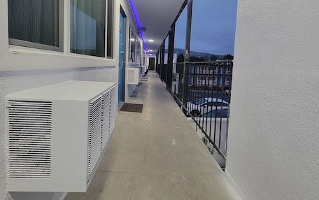 A corridor with air conditioning units, a balcony with a railing, and a view of a street with cars.