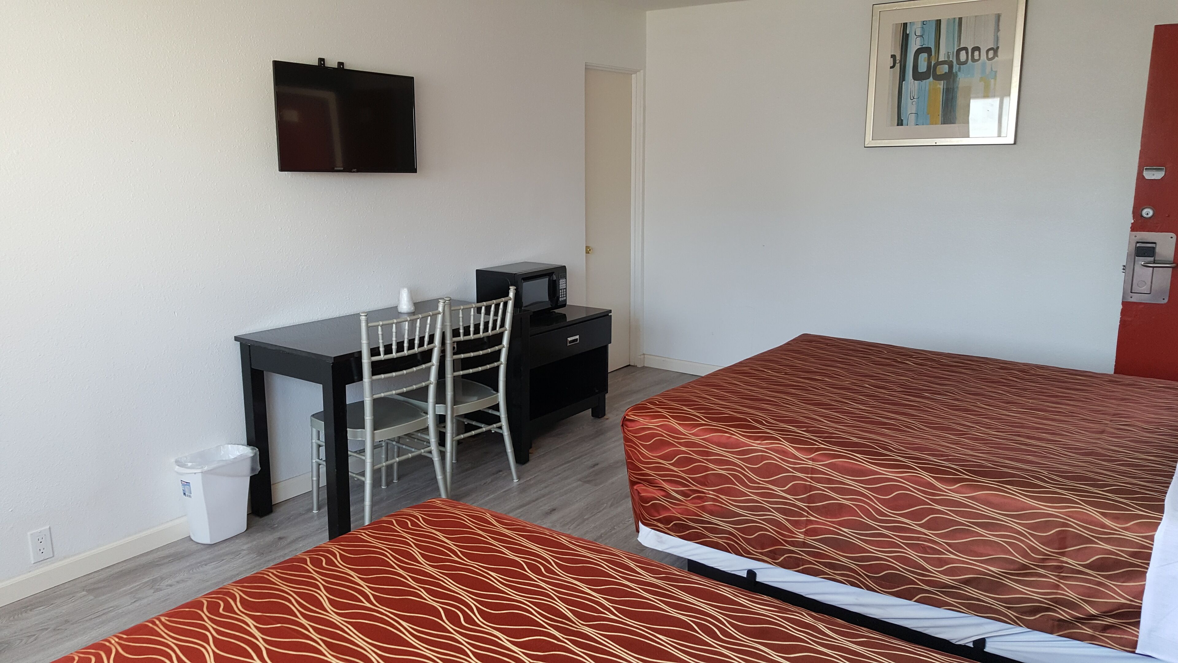A room with a bed, a desk, a chair, a TV, and a trash bin.