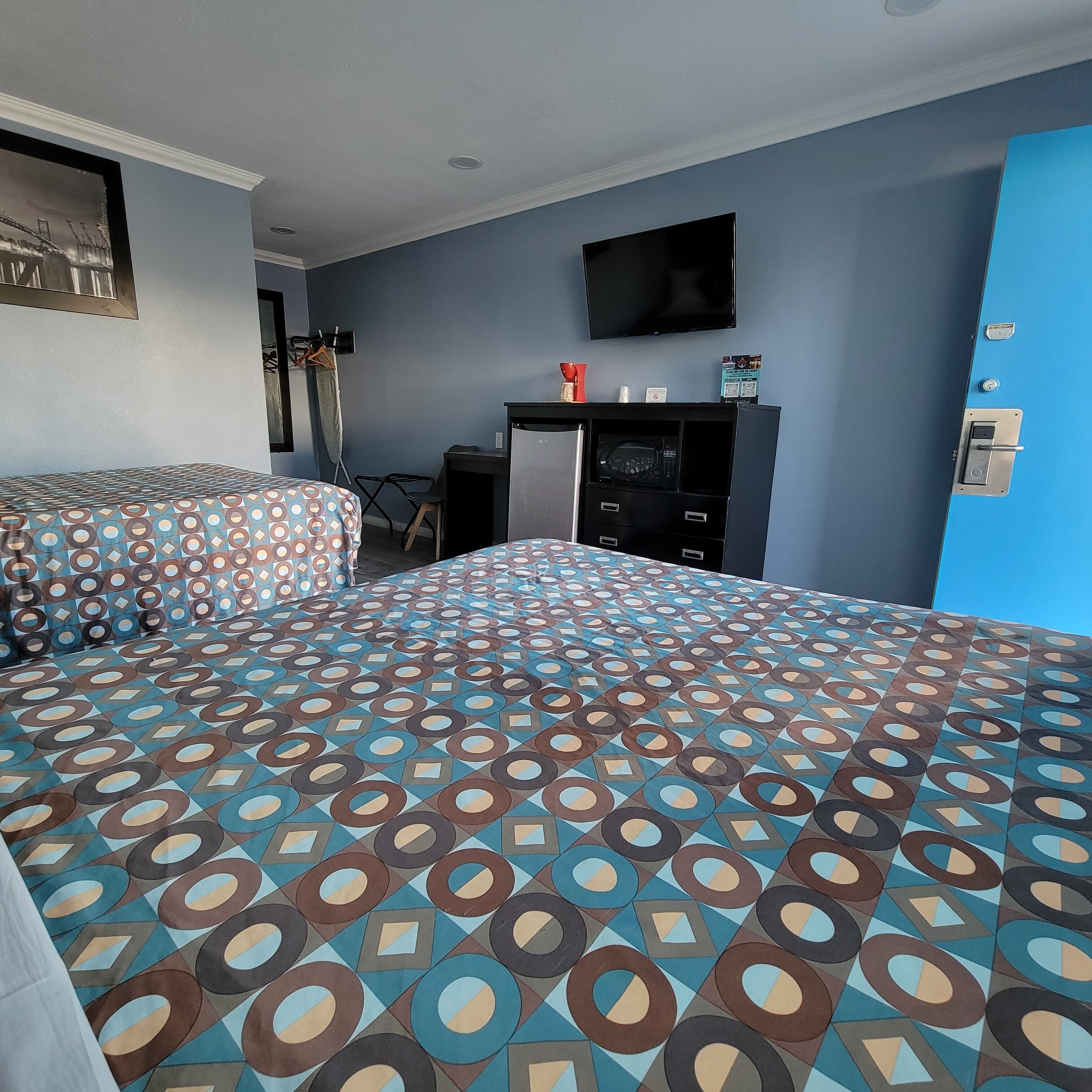 A hotel room with two beds, a desk, a TV, and a minibar.