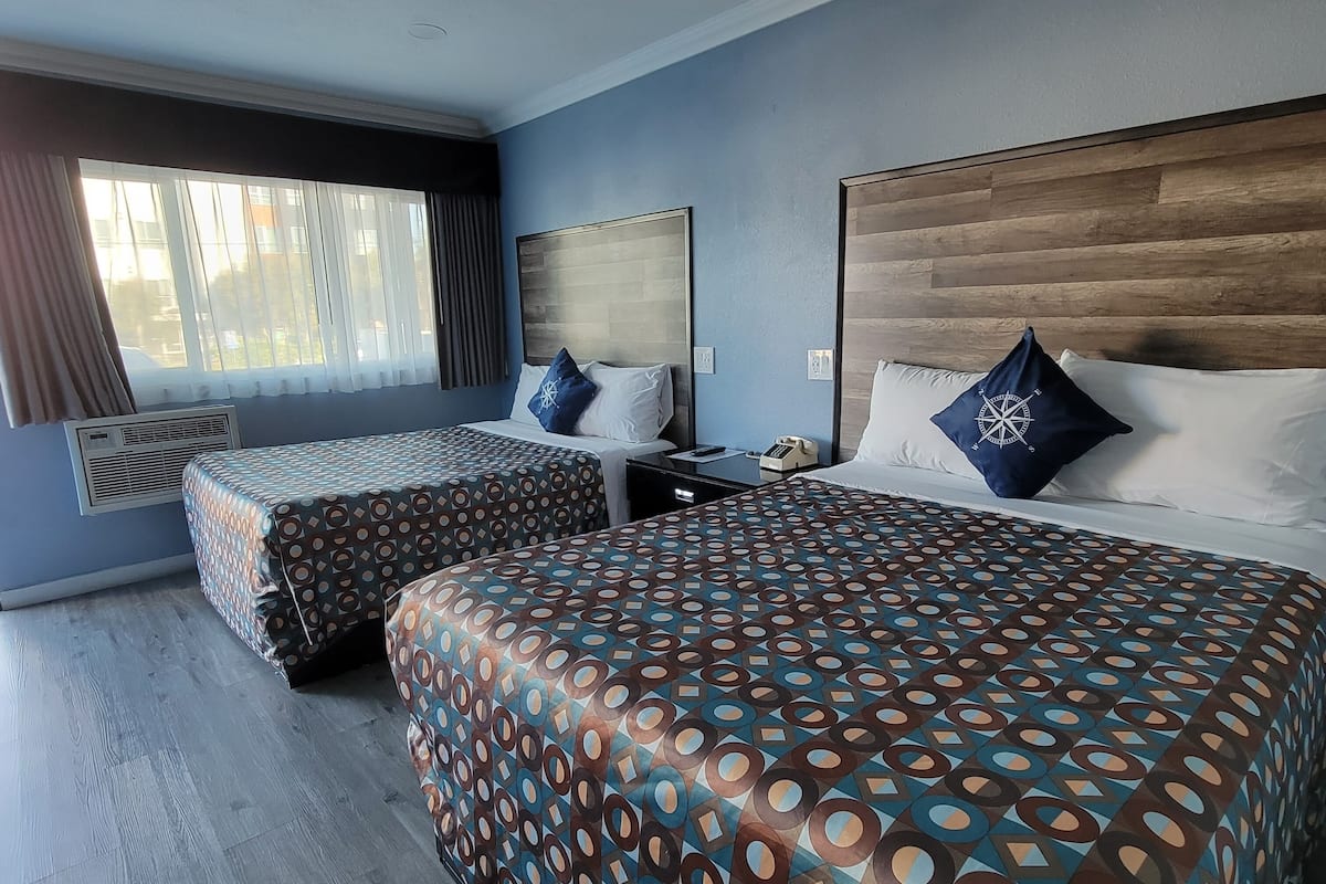 A hotel room with two beds, a large window with curtains, a wooden headboard, and a nightstand with a phone.