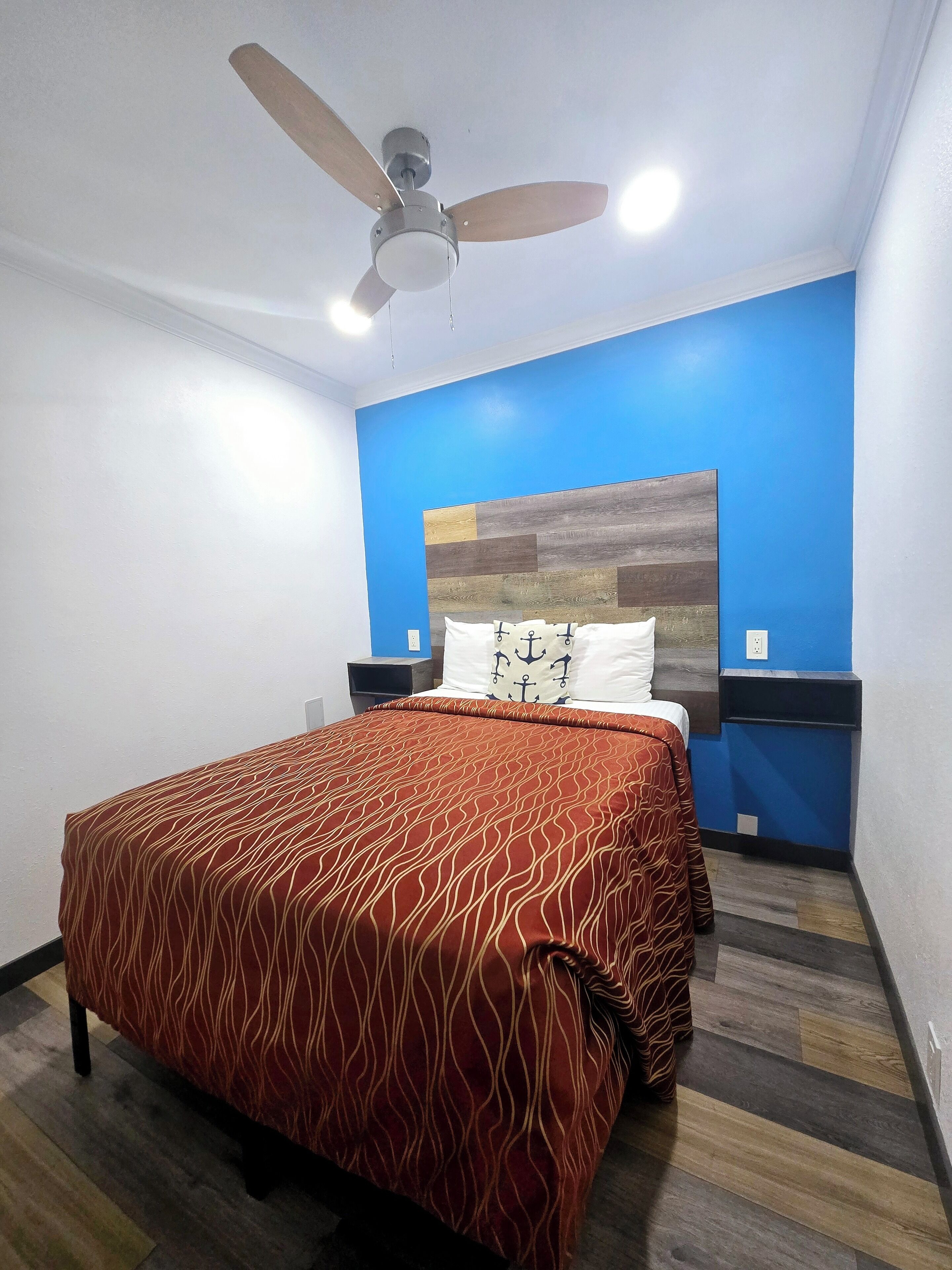 Un dormitorio con cama, ventilador de techo y una pared decorada en azul.