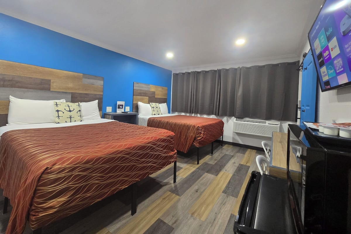 A hotel room with two beds, a desk, a TV, and a window with curtains.