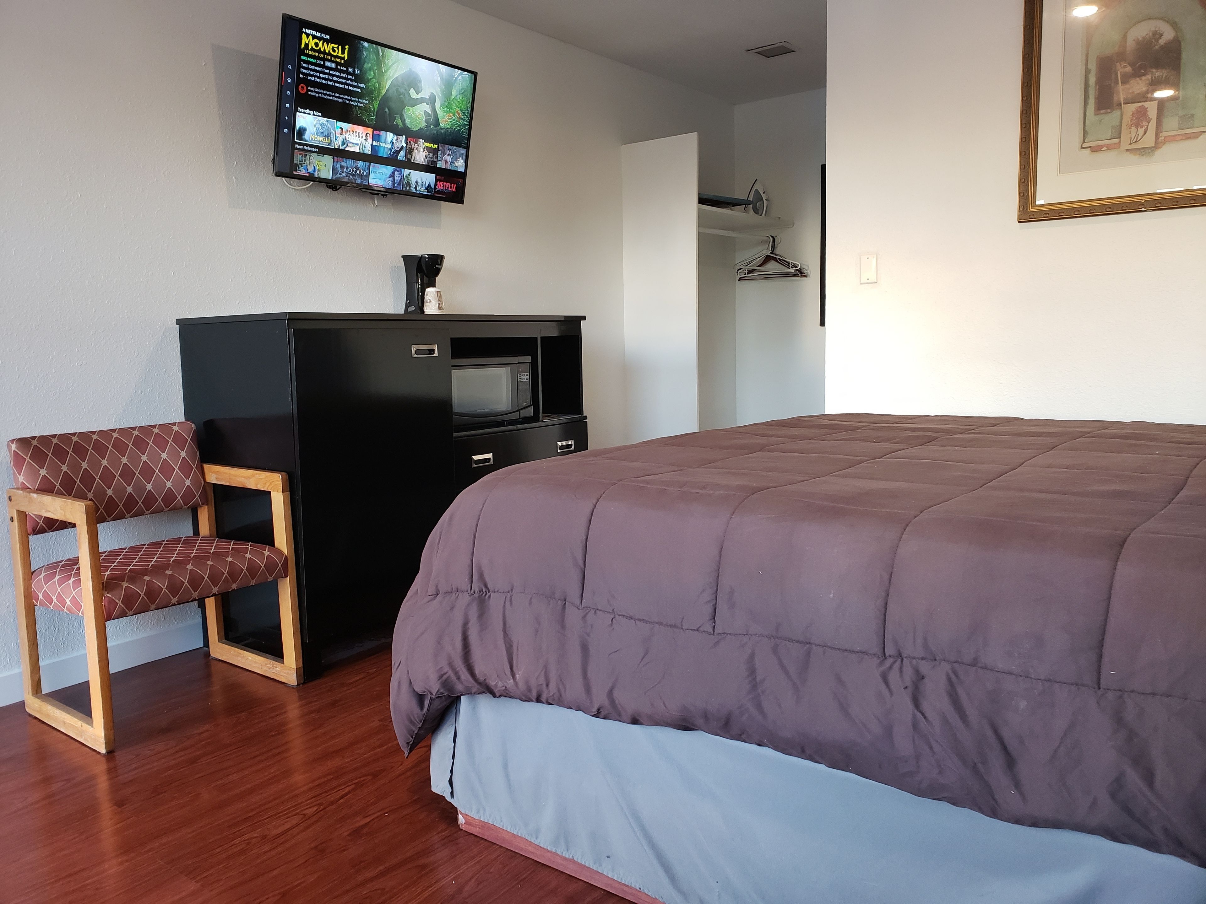 Un dormitorio con cama, televisor montado en la pared, escritorio con microondas y una silla.