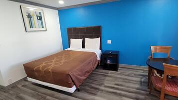 A hotel room with a bed, a nightstand, a chair, and a table.