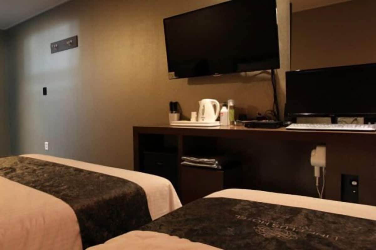 Quarto de hotel com duas camas, uma escrivaninha com computador, televisão e cafeteira.